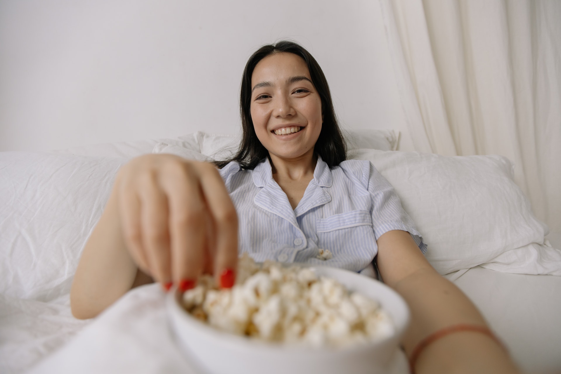 Young woman eating popcorn in bed before going to sleep